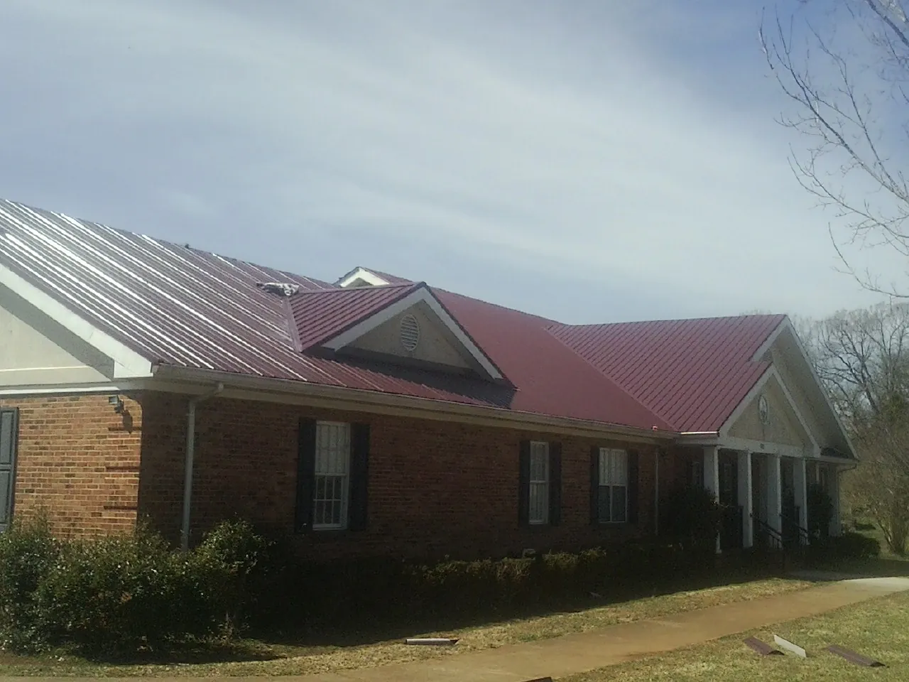 Red metal roof with gabled entries on a long brick building, from a Hail Damage Roof Repair job in Kings Bay