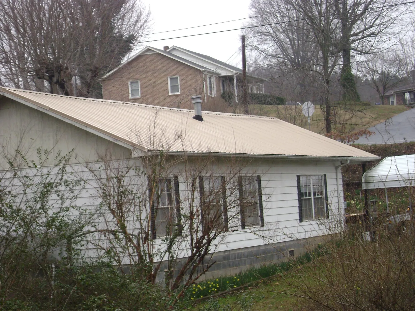 Tan metal roof on a white sided house set into a hillside — Commercial Roofing by Roofing Brothers in Kings Bay